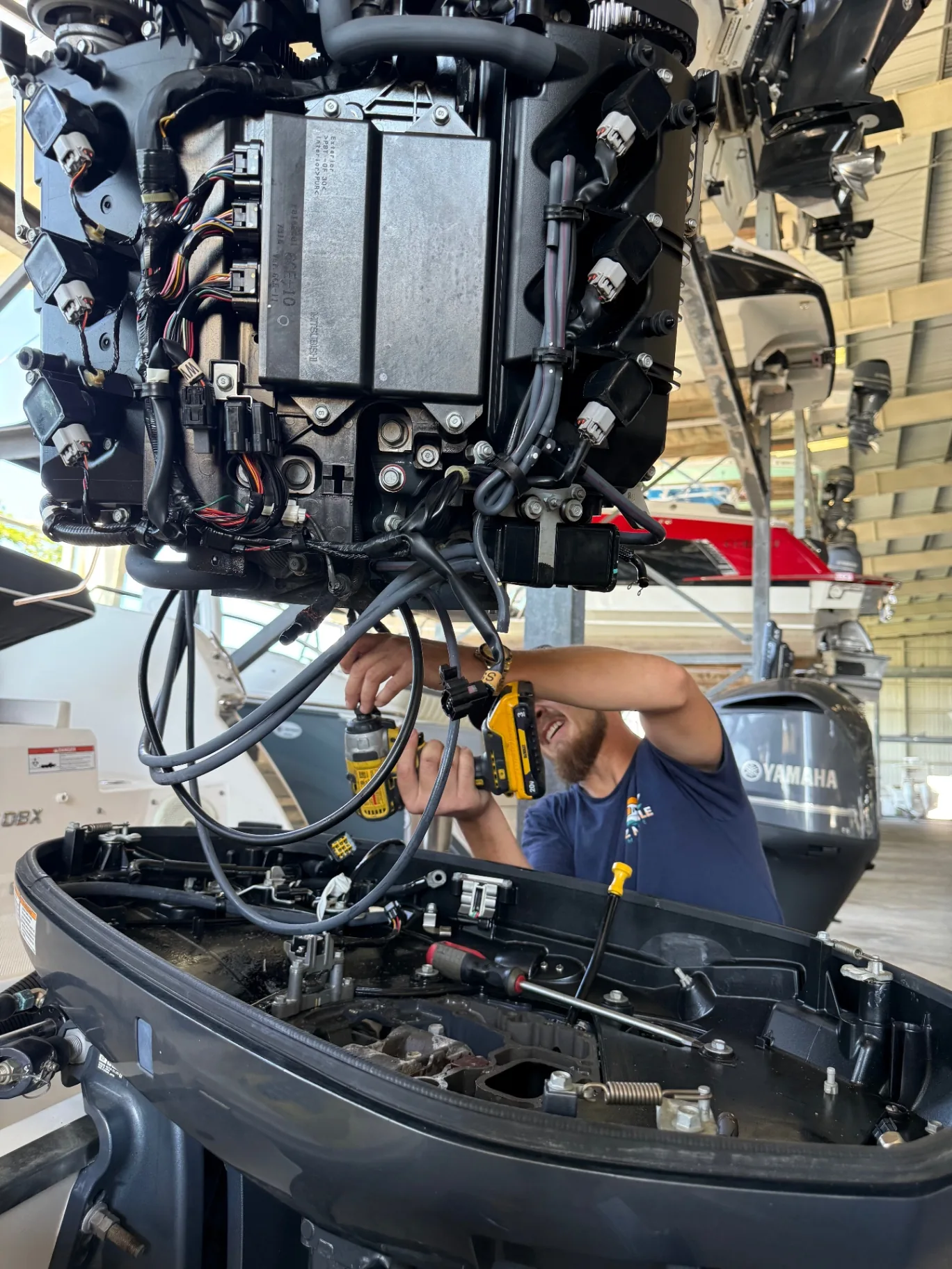 Ethan of EZ Mobile Marine using an impact driver on a hoisted outboard powerhead