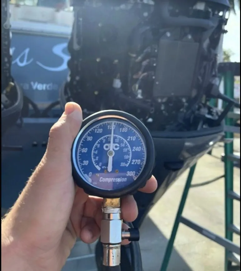 Compression gauge held up in front of an outboard powerhead during diagnostics