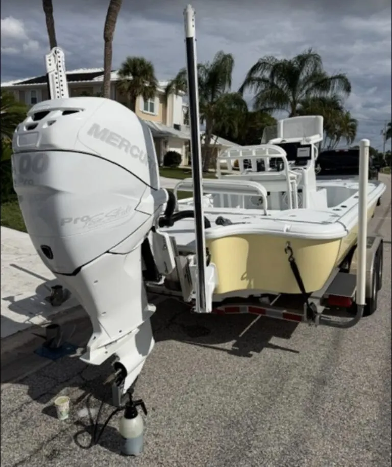 Bay boat on a trailer with outboard being flushed in a residential driveway