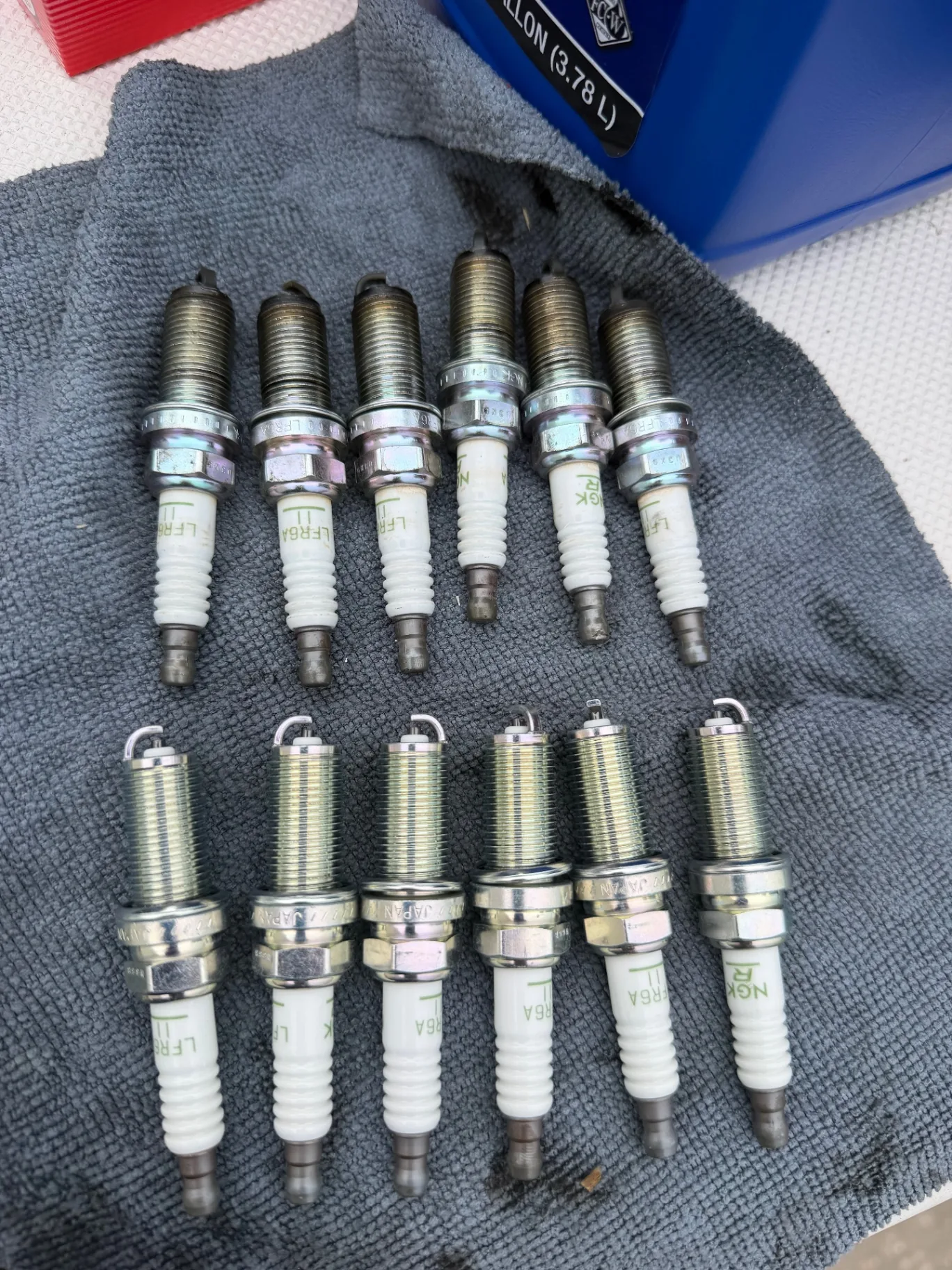 Six worn spark plugs lined up beside six new ones after a 100-hour outboard service