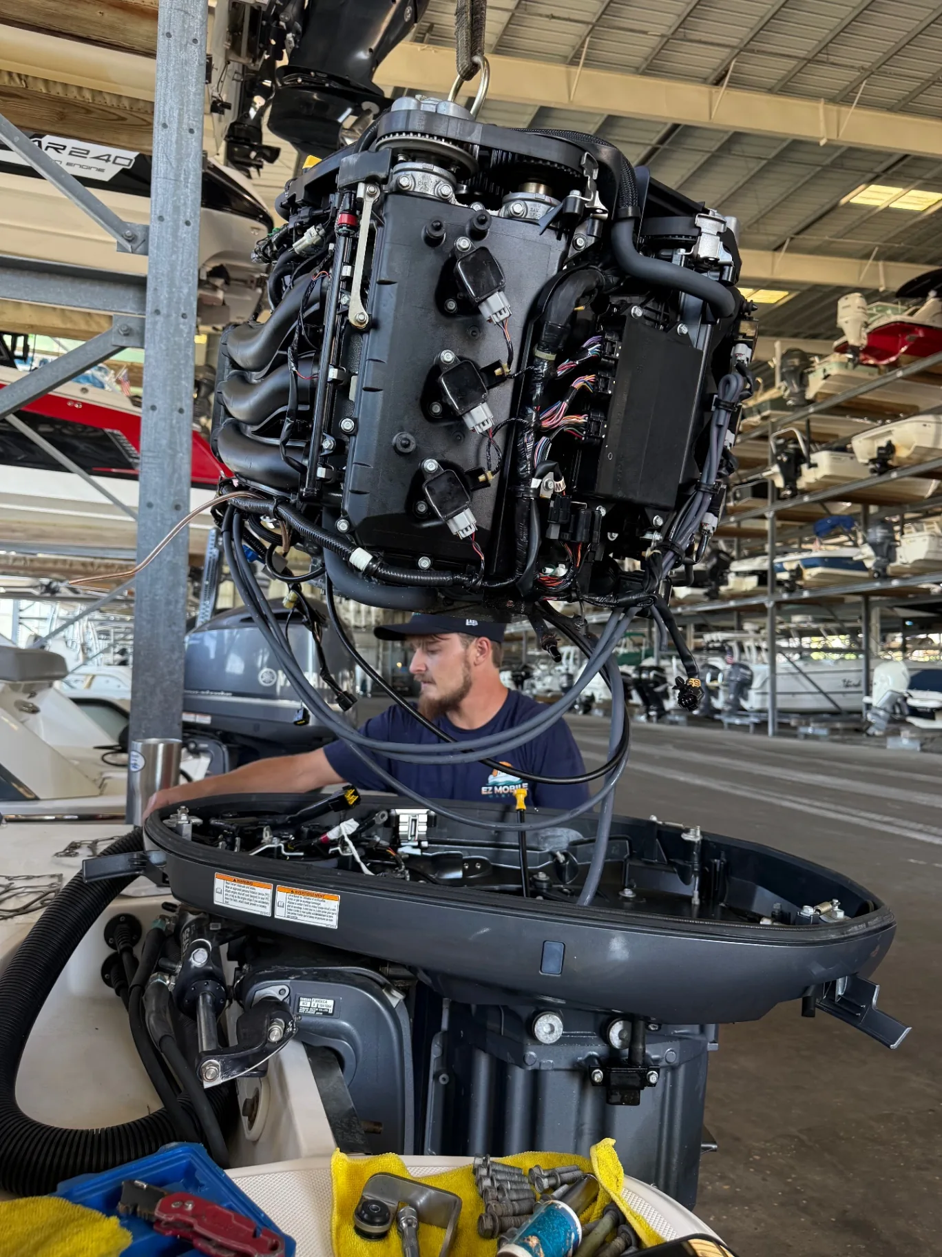 Ethan of EZ Mobile Marine working under a hoisted outboard powerhead in a dry-stack boat shop