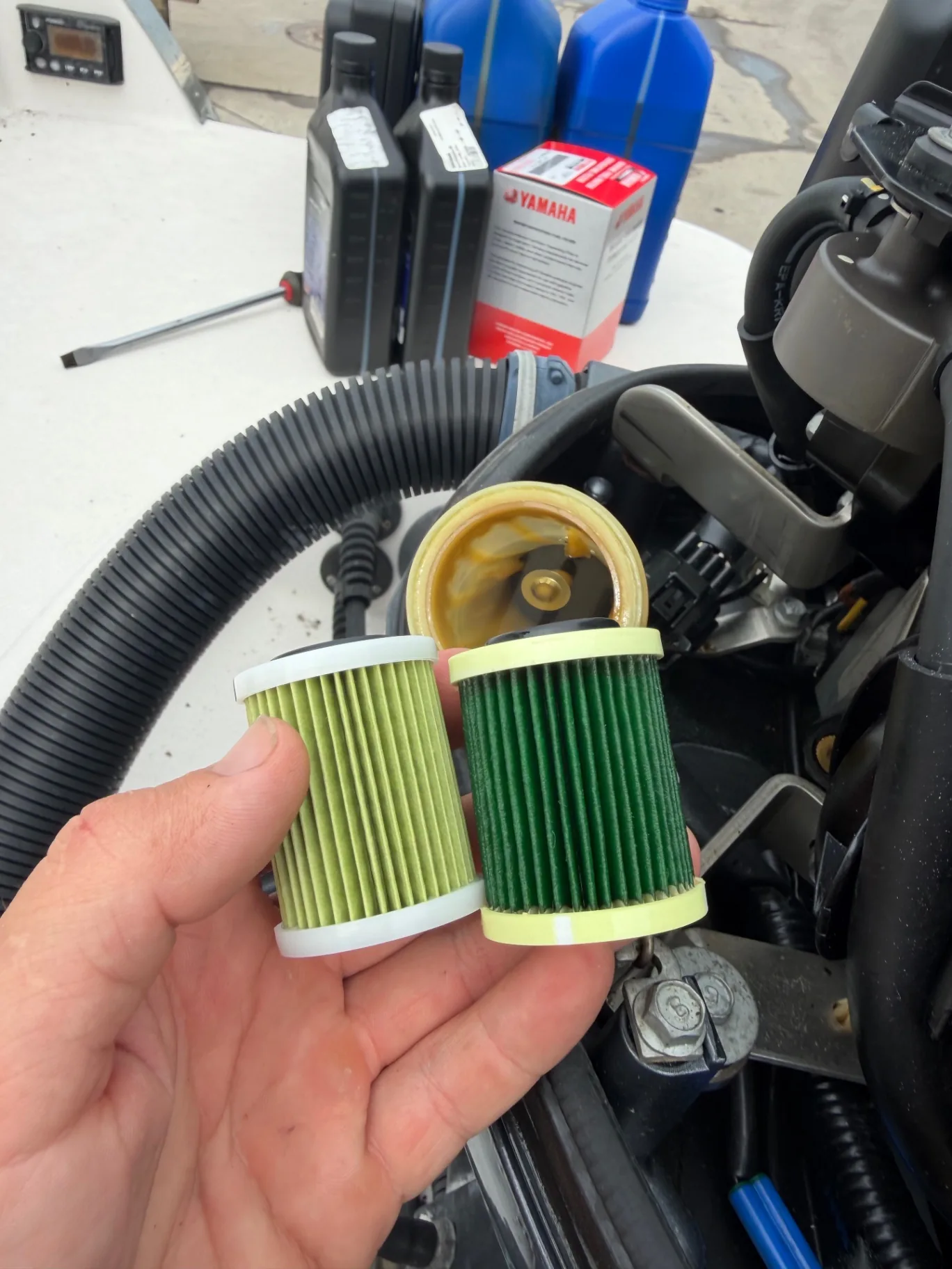 Hand holding a new fuel filter element beside a dirty one during a fuel system service